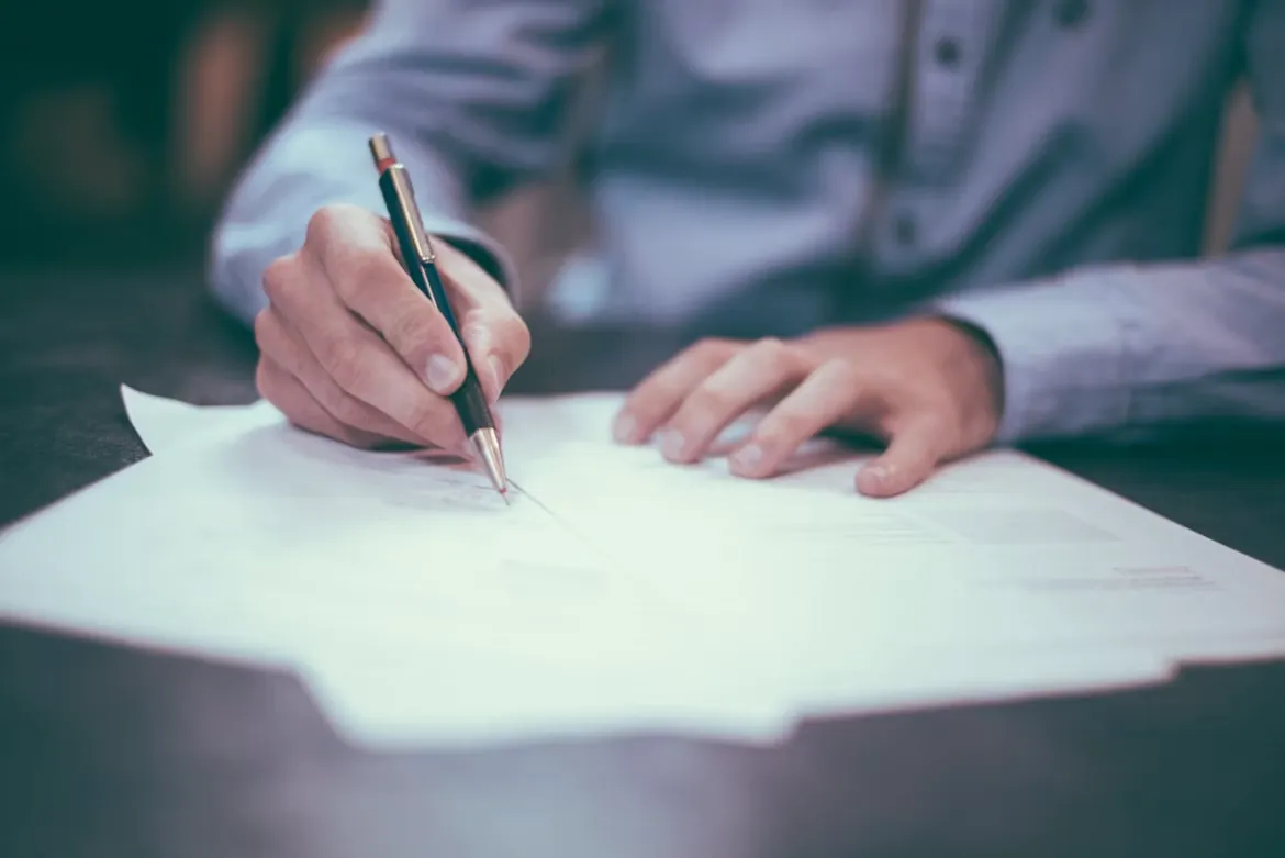 Close-up of a hand signing a paper document with a pen
